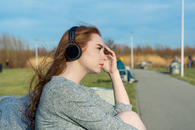 Το νέο, λυπημένο redhead κορίτσι κραυγής την άνοιξη στο πάρκο κοντά στον ποταμό ακούει τη μουσική μέσω των ασύρματων ακουστικών b στοκ φωτογραφία με δικαίωμα ελεύθερης χρήσης Το νέο, λυπημένο redhead κορίτσι κραυγής την άνοιξη στο πάρκο κοντά στον ποταμό ακούει τη μουσική μέσω των ασύρματων ακουστικών b στοκ φωτογραφία με δικαίωμα ελεύθερης χρήσης