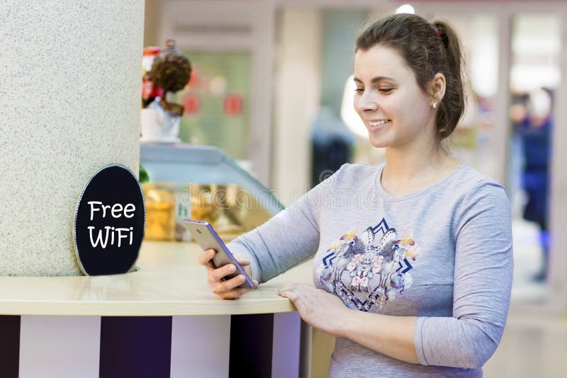 Το νέο όμορφο κορίτσι χρησιμοποιεί το smartphone στην ελεύθερη ζώνη WI Fi στον καφέ λεωφόρων αγορών Ελκυστική ζώνη Wifi γυναικών στοκ φωτογραφία με δικαίωμα ελεύθερης χρήσης