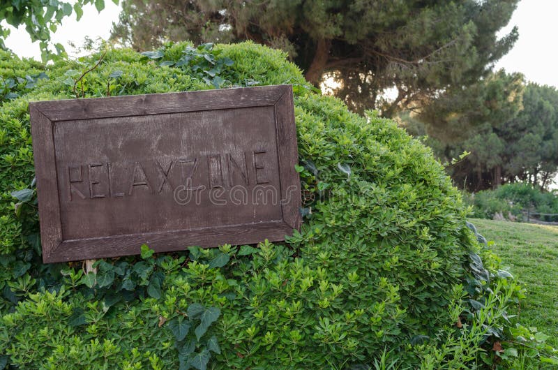 Το ξύλινο σημάδι χαλαρώνει τη ζώνη στο μεγάλο πράσινο θάμνο στο πάρκο στοκ φωτογραφίες με δικαίωμα ελεύθερης χρήσης Το ξύλινο σημάδι χαλαρώνει τη ζώνη στο μεγάλο πράσινο θάμνο στο πάρκο στοκ φωτογραφίες με δικαίωμα ελεύθερης χρήσης