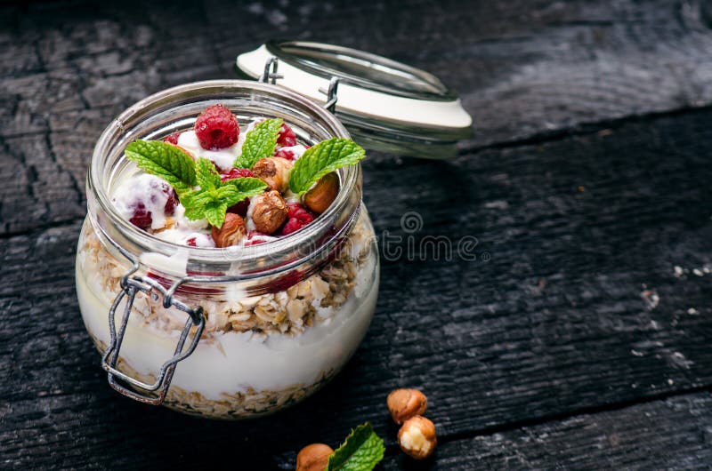 Το πλήρες βάζο του muesli, γιαούρτι, σμέουρα, καρύδια στο Μαύρο, έκαψε τον ξύλινο πίνακα Σπιτικά τρόφιμα δημητριακών προγευμάτων στοκ φωτογραφία