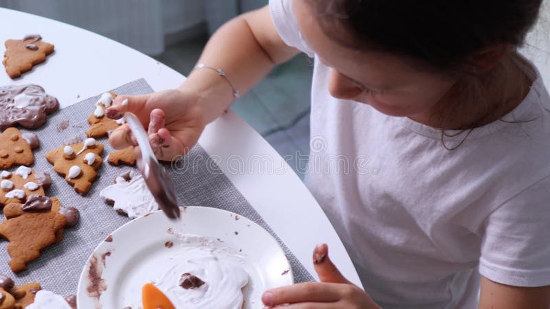 το παιδί διακοσμεί μπισκότα διακοπών με λευκό και σοκολατένιο γυαλί