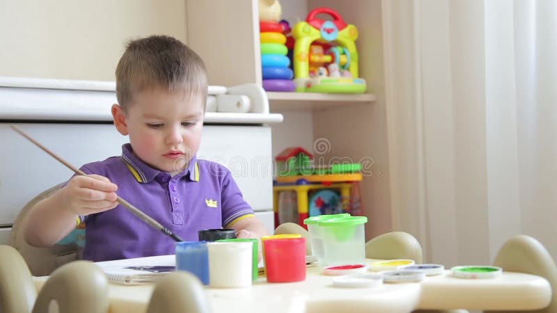 Το παιδί στα χρώματα παιδικών σταθμών με μια βούρτσα με τα χρωματισμένα χρώματα