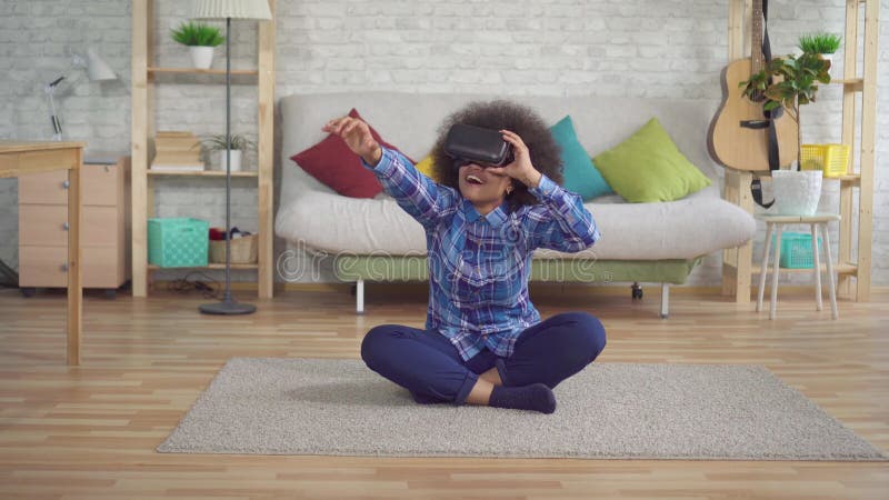 Το πορτρέτο της εκφραστικής θετικής νέας γυναίκας αφροαμερικάνων χρησιμοποιεί τα γυαλιά Vr και την εικονική τεχνολογία στο καθιστ