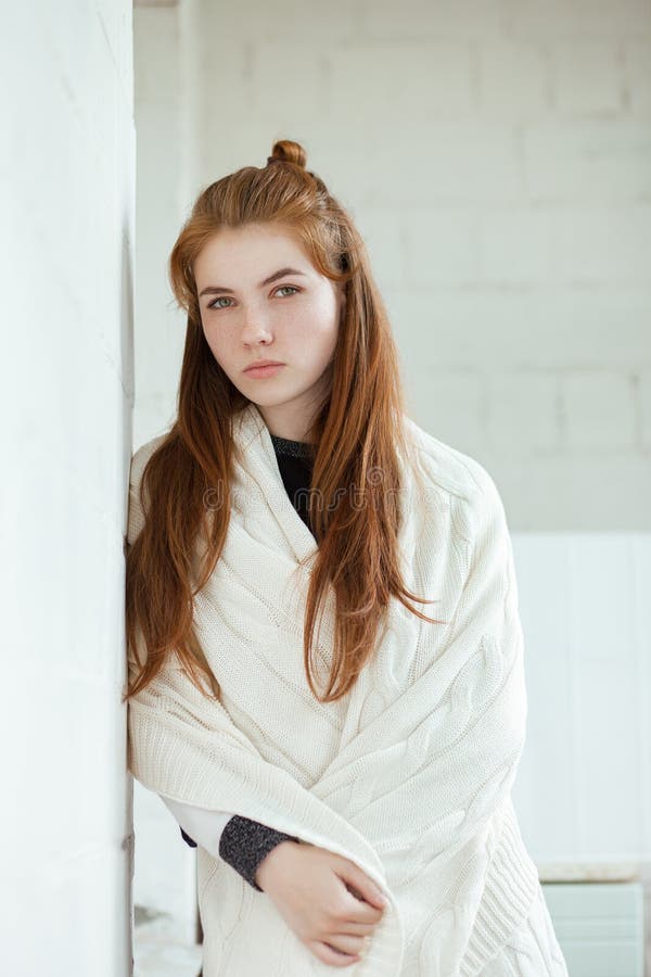 Το πορτρέτο της νέας λατρευτής redhead γυναίκας τύλιξε σε μια άσπρη πλεκτή γενική τοποθέτηση κοντά στο άσπρο εσωτερικό φυσικό φως στοκ εικόνα με δικαίωμα ελεύθερης χρήσης