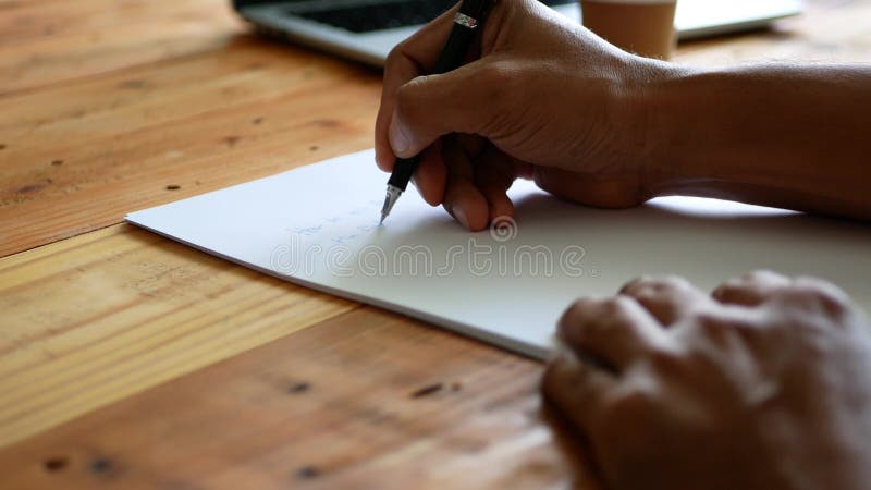 Το χέρι ενός άντρα να γράφει σε μια λευκή βίβλο πάνω σε ένα τραπέζι με ένα φλιτζάνι καφέ και ένα σημειωματάριο κοντά απόθεμα βίντεο Το χέρι ενός άντρα να γράφει σε μια λευκή βίβλο πάνω σε ένα τραπέζι με ένα φλιτζάνι καφέ και ένα σημειωματάριο κοντά απόθεμα βίντεο