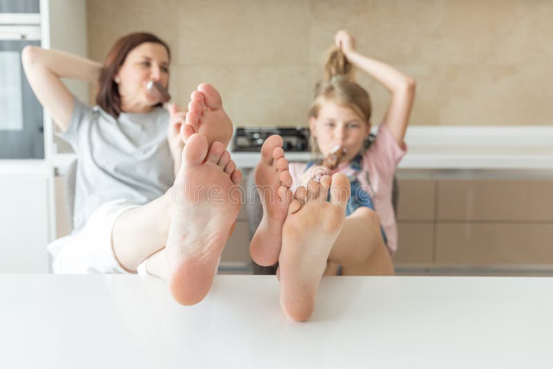 Το χαριτωμένο κορίτσι και η μητέρα της χαμογελούν τρώγοντας το παγωτό στην κουζίνα με τα πόδια σε έναν πίνακα στοκ φωτογραφίες