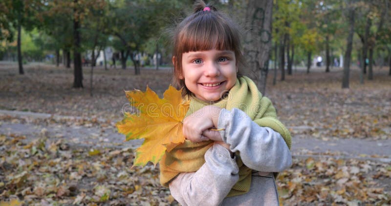 Το χαριτωμένο μικρό κορίτσι καλύπτει το πρόσωπό της με το κίτρινο φύλλο και το χαμόγελο στη κάμερα στην κινηματογράφηση σε πρώτο