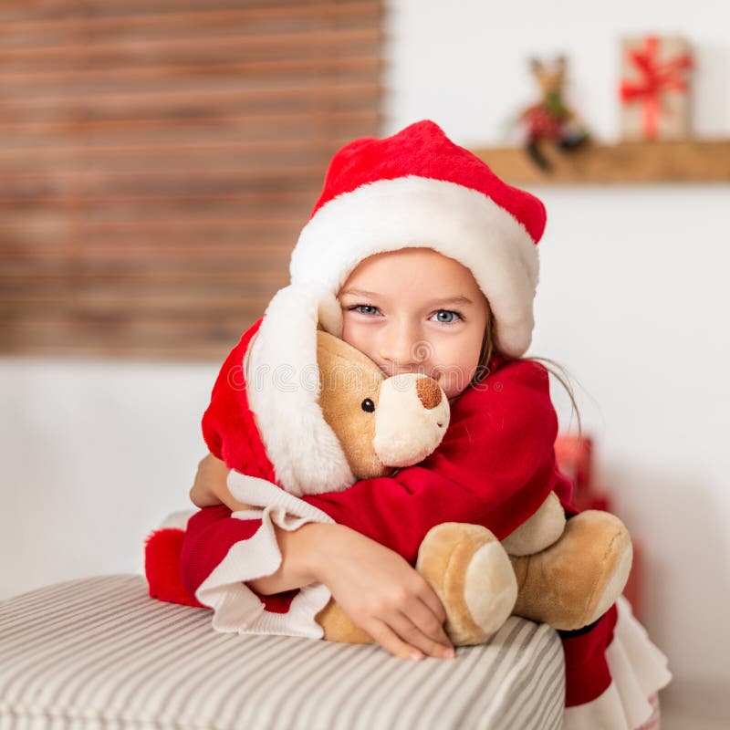 Το χαριτωμένο νέο κορίτσι που φορά το καπέλο santa που αγκαλιάζει το χριστουγεννιάτικο δώρο της, μαλακό παιχνίδι teddy αντέχει Ευ στοκ εικόνες