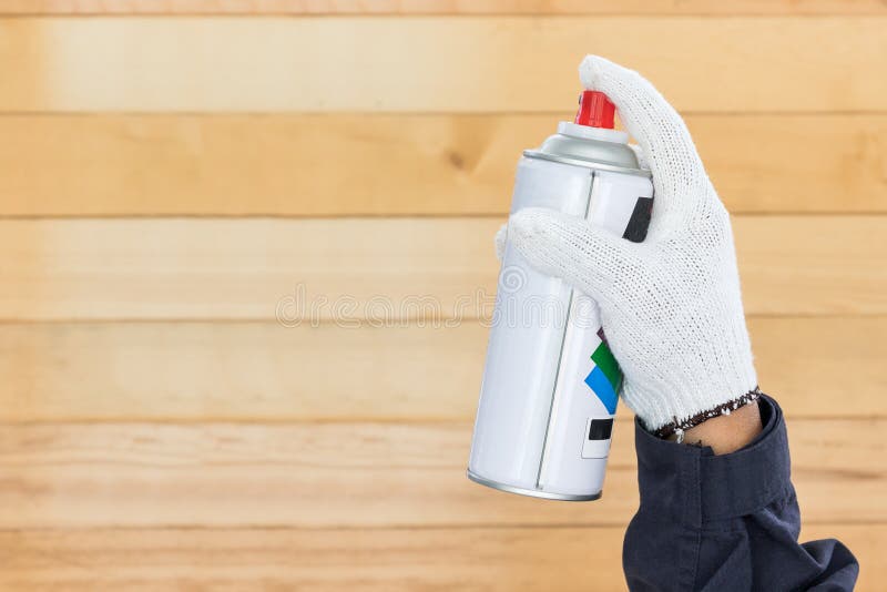 Working hand in glove holding spray paint can with wall wood background. Working hand in glove holding spray paint can with wall wood background