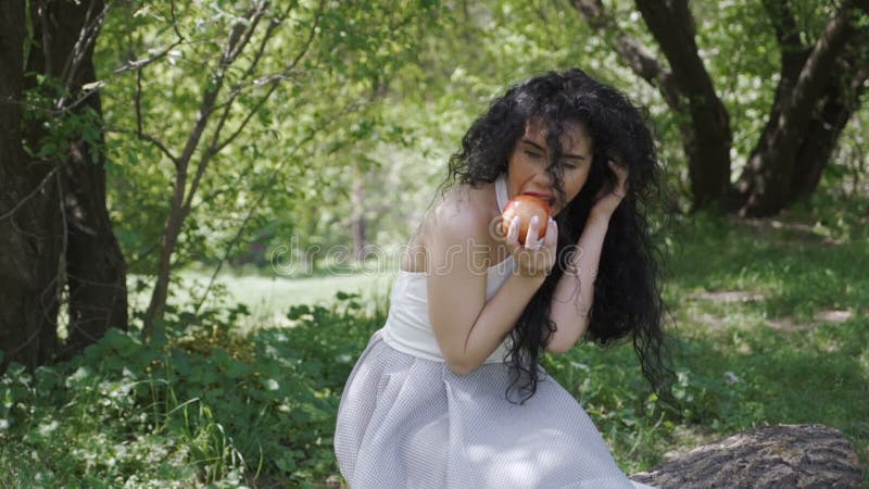 Το όμορφο brunette τρώει το κόκκινο μήλο στον κήπο
