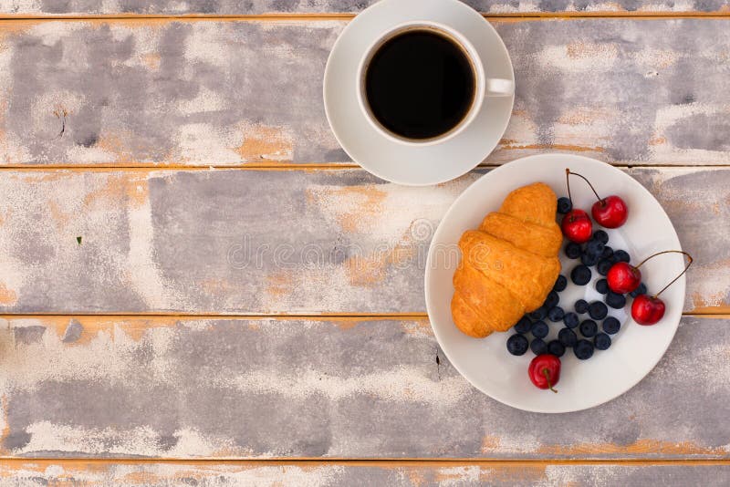 Τοπ άποψη ενός εύγευστου προγεύματος με τα croissants, τον καφέ και τα βακκίνια και το κεράσι στον πίνακα στοκ φωτογραφίες Τοπ άποψη ενός εύγευστου προγεύματος με τα croissants, τον καφέ και τα βακκίνια και το κεράσι στον πίνακα στοκ φωτογραφίες