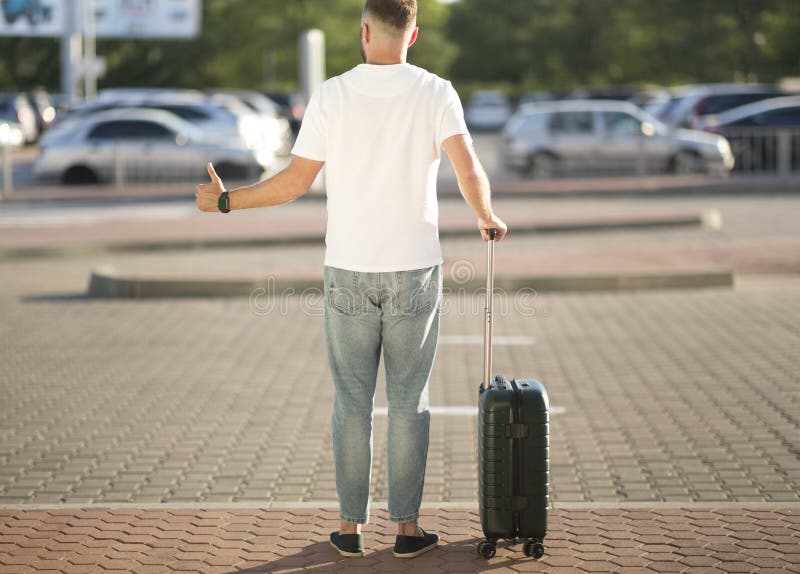 Arriving Home Concept. Tourist trying to catch taxi, standing with baggage and showing thumbs up, copyspace, back view. Arriving Home Concept. Tourist trying to catch taxi, standing with baggage and showing thumbs up, copyspace, back view