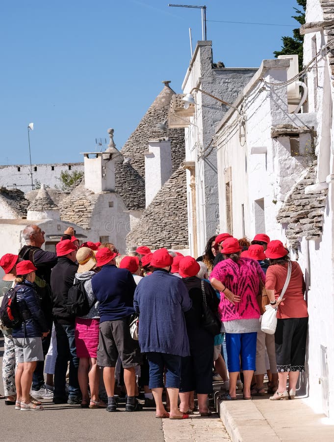 Τουρίστες στην πόλη Puglian Alberobello, που εξετάζει και που φωτογραφίζει τα παραδοσιακά σπίτια trulli ξηρών πετρών που είναι μο στοκ εικόνες με δικαίωμα ελεύθερης χρήσης Τουρίστες στην πόλη Puglian Alberobello, που εξετάζει και που φωτογραφίζει τα παραδοσιακά σπίτια trulli ξηρών πετρών που είναι μο στοκ εικόνες με δικαίωμα ελεύθερης χρήσης