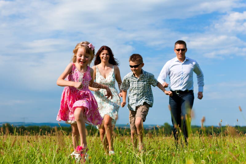 Happy family - mother, father, children - running over a green meadow in summer kicking a soccer ball. Happy family - mother, father, children - running over a green meadow in summer kicking a soccer ball