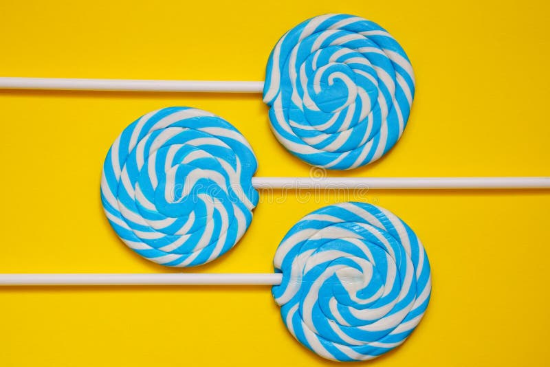 Τρία άσπρα και μπλε lollipops στο κίτρινο υπόβαθρο στοκ φωτογραφία Τρία άσπρα και μπλε lollipops στο κίτρινο υπόβαθρο στοκ φωτογραφία