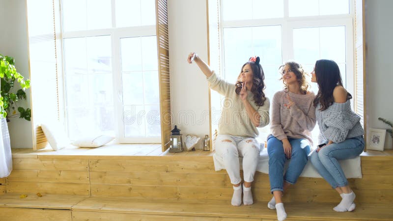 Τρία όμορφα κορίτσια πυροβολούν selfie καθμένος στο παράθυρο Φίλες που έχουν το γέλιο διασκέδασης στην κρεβατοκάμαρα