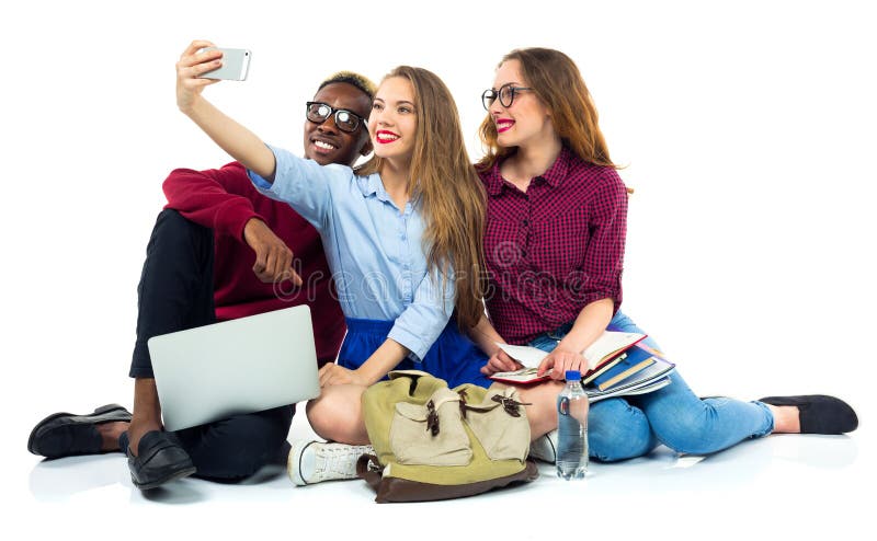 Τρεις ευτυχείς σπουδαστές με τα βιβλία, lap-top, τοποθετούν σε σάκκο και κάνουν selfie