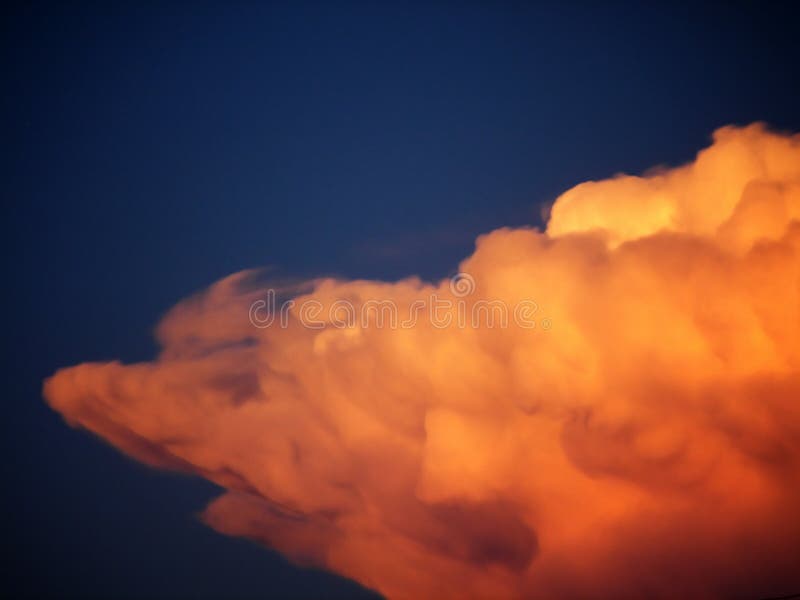 A puffy orange colored cloud against a deep blue sky. A puffy orange colored cloud against a deep blue sky