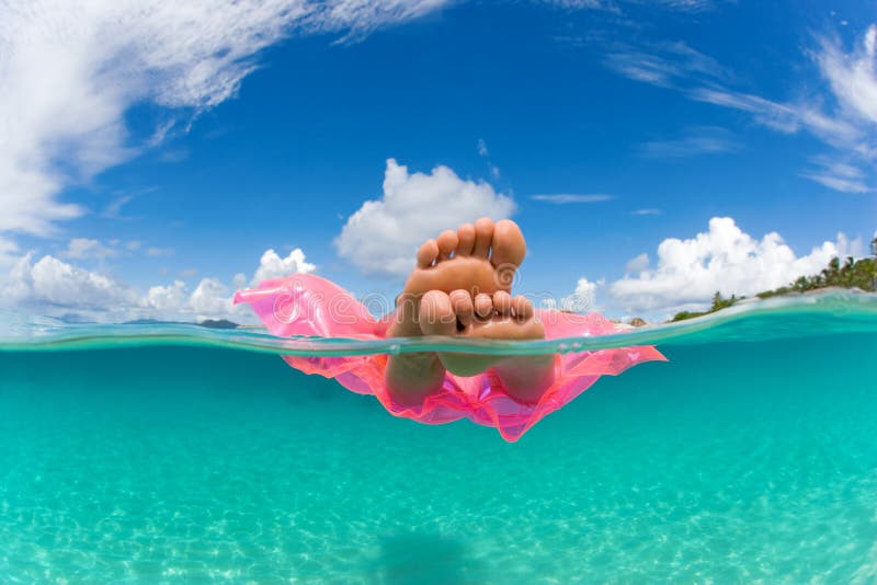 Woman floating on inflatable raft in tropical water with feet showing under over. Woman floating on inflatable raft in tropical water with feet showing under over