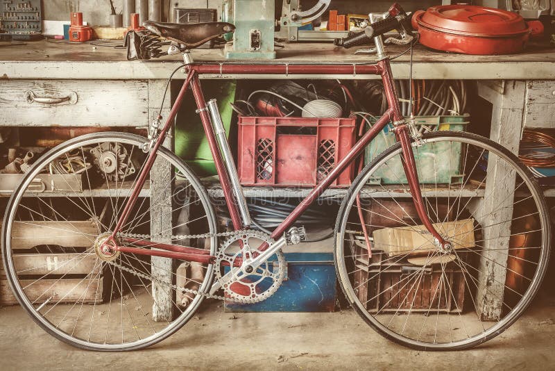 Τρύγος που συναγωνίζεται bycicle μπροστά από έναν παλαιό πάγκο εργασίας με τα εργαλεία στοκ εικόνες Τρύγος που συναγωνίζεται bycicle μπροστά από έναν παλαιό πάγκο εργασίας με τα εργαλεία στοκ εικόνες