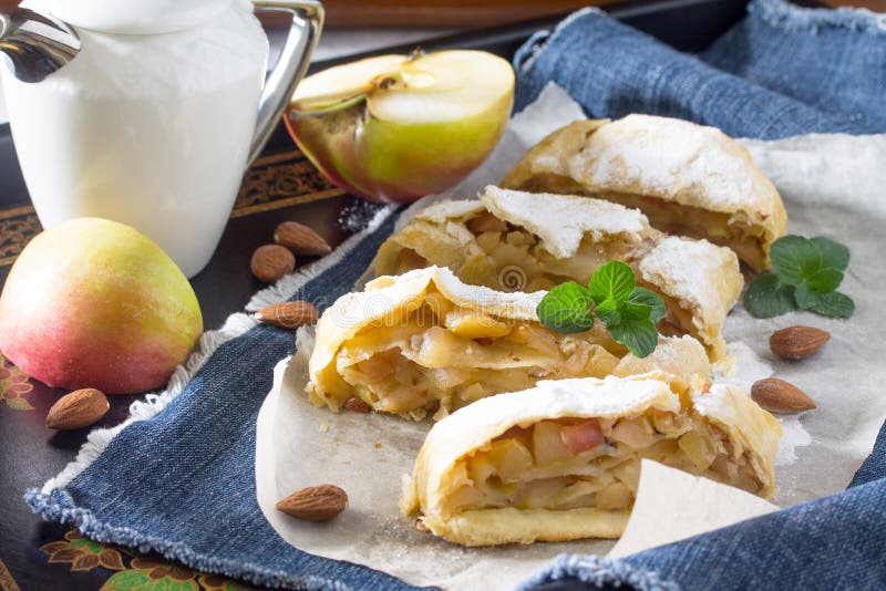 Tea and sliced homemade apple strudel with fresh apples, nuts and powdered sugar on a vintage wooden background. .Tea and sliced homemade apple strudel with fresh apples, nuts and powdered sugar on a vintage wooden background