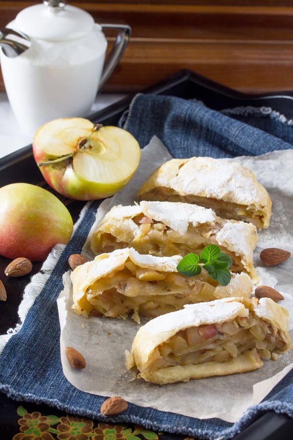 Tea and sliced homemade apple strudel with fresh apples, nuts and powdered sugar on a vintage wooden background. Tea and sliced homemade apple strudel with fresh apples, nuts and powdered sugar on a vintage wooden background