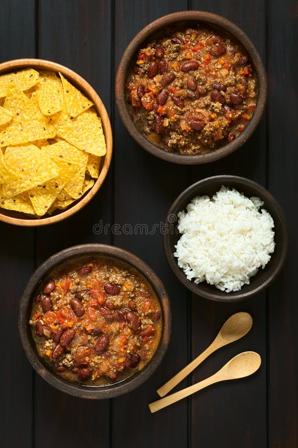 Overhead shot of two bowls of chili con carne with rice and tortilla chips, photographed on dark wood with natural light. Overhead shot of two bowls of chili con carne with rice and tortilla chips, photographed on dark wood with natural light