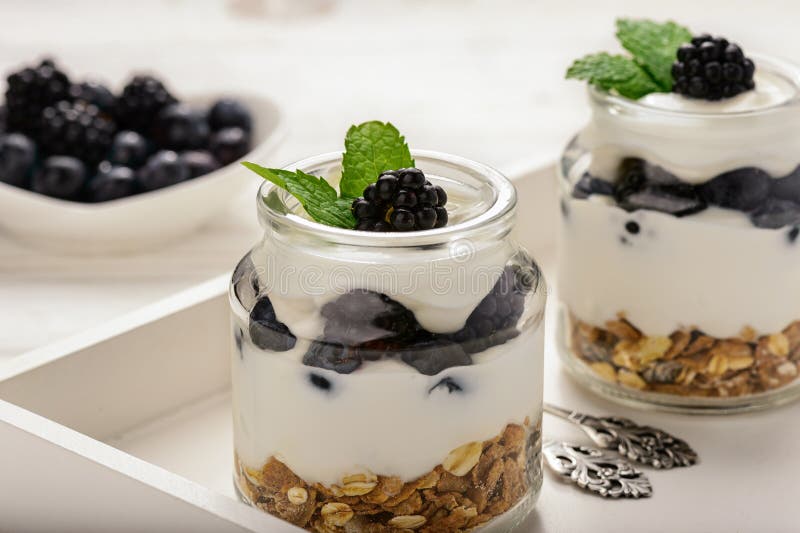 Υγιές επιδόρπιο γιαουρτιού με το muesli, τα βατόμουρα και τα βακκίνια στον άσπρο ξύλινο πίνακα στοκ εικόνες Υγιές επιδόρπιο γιαουρτιού με το muesli, τα βατόμουρα και τα βακκίνια στον άσπρο ξύλινο πίνακα στοκ εικόνες