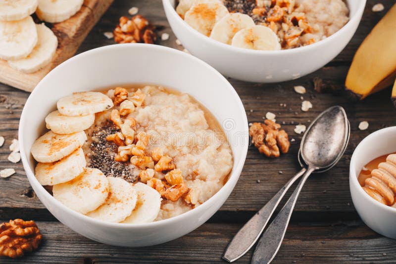 Υγιές κύπελλο προγευμάτων oatmeal με την μπανάνα, τα ξύλα καρυδιάς, τους σπόρους chia και το μέλι στοκ εικόνες