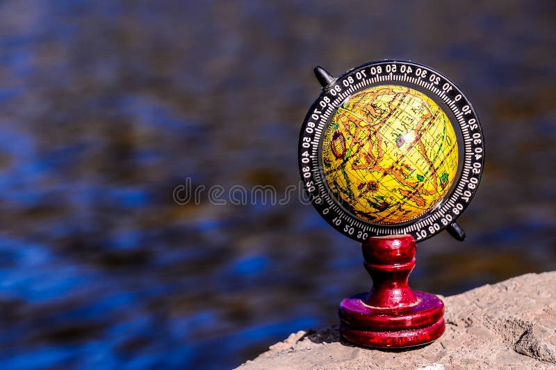 A globe sits on a rock by a body of water. The globe is yellow and black and has a red base. The scene is peaceful and serene, with the water and the globe creating a sense of calm and tranquility, real image. A globe sits on a rock by a body of water. The globe is yellow and black and has a red base. The scene is peaceful and serene, with the water and the globe creating a sense of calm and tranquility, real image