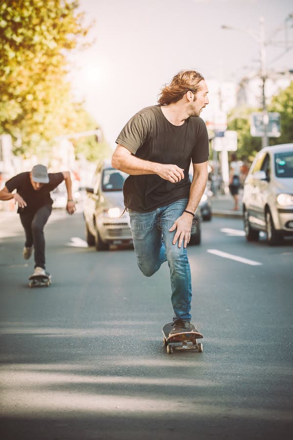 Υπέρ skateboard δύο σαλάχι γύρου αναβατών μέσω των αυτοκινήτων στην οδό στοκ εικόνες Υπέρ skateboard δύο σαλάχι γύρου αναβατών μέσω των αυτοκινήτων στην οδό στοκ εικόνες