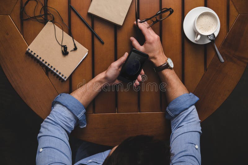 υπερυψωμένη άποψη του ατόμου που χρησιμοποιεί το iphone στον ξύλινο πίνακα με τον καφέ στοκ εικόνα με δικαίωμα ελεύθερης χρήσης