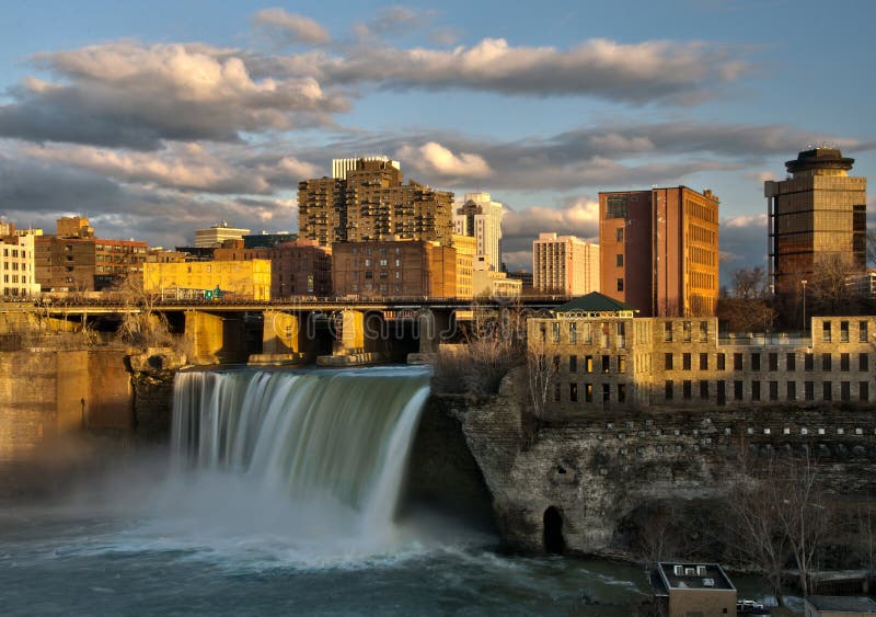 A sunset view of the High Falls, a waterfall on the Genesee River that passes through the historic downtown section of Rochester, New York. A sunset view of the High Falls, a waterfall on the Genesee River that passes through the historic downtown section of Rochester, New York