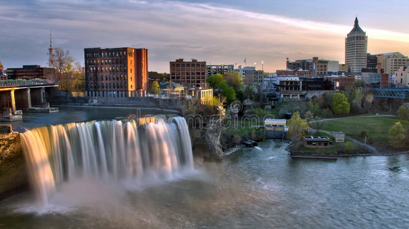 A panoramic sunset view of the High Falls, a waterfall on the Genesee River that passes through the historic downtown section of Rochester, New York. A panoramic sunset view of the High Falls, a waterfall on the Genesee River that passes through the historic downtown section of Rochester, New York