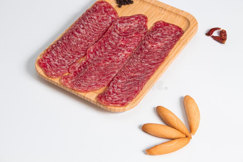φέτες chorizo συνοδευόμενες από φέτες ψωμιού σε ξύλινη σανίδα με λευκό φόντο και ελαφριά βάση