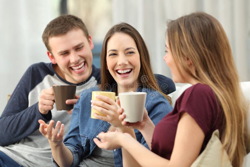 Three happy friends talking and laughing loud holding drinks sitting on a sofa in the living room at home. Three happy friends talking and laughing loud holding drinks sitting on a sofa in the living room at home