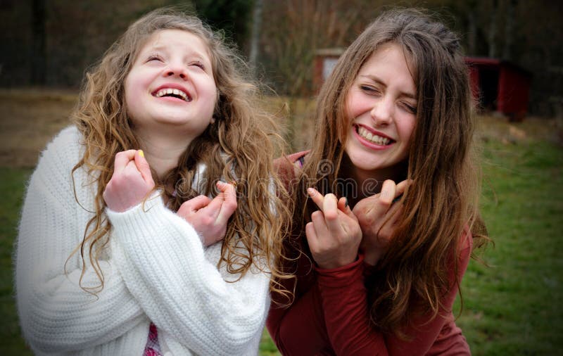 Two pretty young girls intensely just wishing and hoping with fingers crossed, both with long blond hair and smiling. Shallow depth of field. Two pretty young girls intensely just wishing and hoping with fingers crossed, both with long blond hair and smiling. Shallow depth of field.