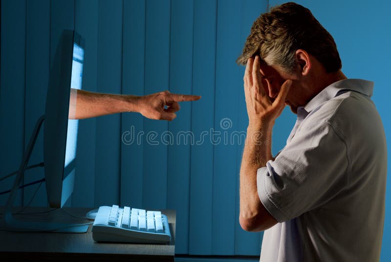 Severely distraught man sitting in front of a computer with a judgmental hand pointing at him from within the computer monitor. Cyber bully concept. Severely distraught man sitting in front of a computer with a judgmental hand pointing at him from within the computer monitor. Cyber bully concept.