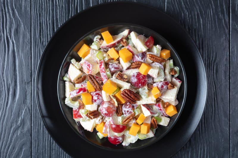 Fresh apple salad with grapes, celery, cheddar cheese and pecan nuts with mayonnaise based dressing on black plates on a wooden table, flatlay, macro. Fresh apple salad with grapes, celery, cheddar cheese and pecan nuts with mayonnaise based dressing on black plates on a wooden table, flatlay, macro