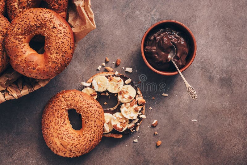 Φρέσκο σπιτικό bagel με την μπανάνα, την κρέμα σοκολάτας και το αμύγδαλο σε ένα σκοτεινό αγροτικό υπόβαθρο r στοκ φωτογραφία με δικαίωμα ελεύθερης χρήσης Φρέσκο σπιτικό bagel με την μπανάνα, την κρέμα σοκολάτας και το αμύγδαλο σε ένα σκοτεινό αγροτικό υπόβαθρο r στοκ φωτογραφία με δικαίωμα ελεύθερης χρήσης