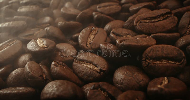 φρυγμένος καφές κουκιά. αρωματικοί κόκκοι καφέ μετακινούνται αργά κινηματογραφημένοι με σκούρο βασικό καπνό που προέρχεται από