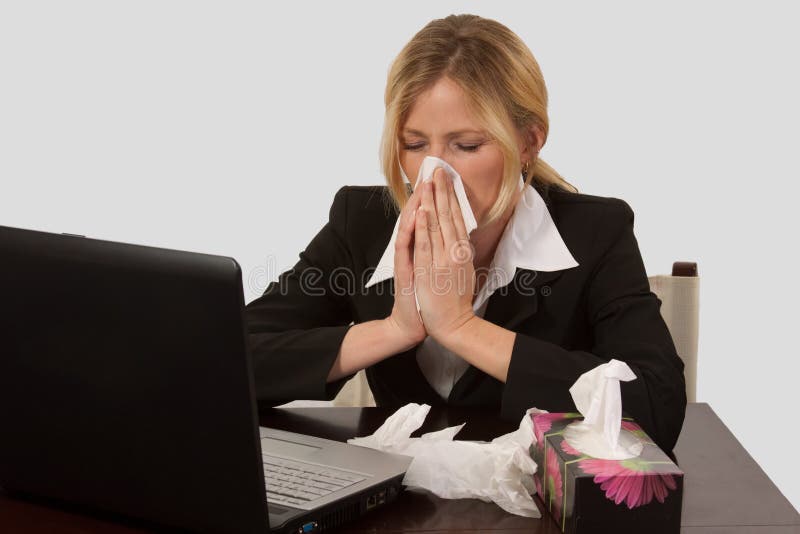 Blond caucasian woman wearing business attire sitting in front of laptop computer with a box of tissues blowing her nose. Blond caucasian woman wearing business attire sitting in front of laptop computer with a box of tissues blowing her nose
