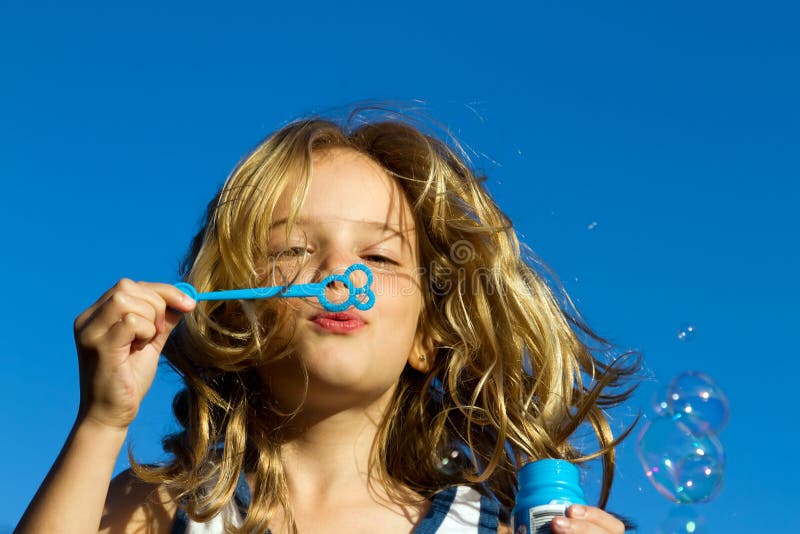 A lovely young girl blowing bubbles against a vibrant blue sky. A lovely young girl blowing bubbles against a vibrant blue sky.