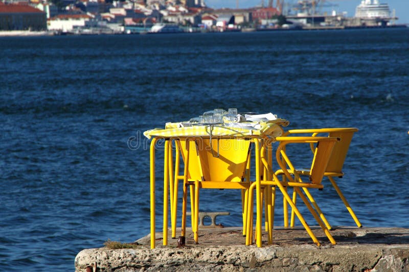 φωτεινό κίτρινο εξωτερικό καφέ τραπέζι και καρέκλες δίπλα στο νερό με φόντο το τοπίο στοκ φωτογραφίες