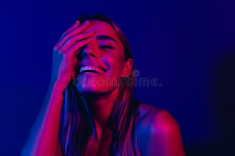 Φωτεινό πορτρέτο μιας νεαρής γυναίκας που χαμογελάει με μπλε και ροζ φώτα. Πορτρέτο μιας νεαρής γυναίκας φωτισμένη από φώτα νέον που εκφράζουν χαρά και γέλιο με ένα μοντέρνο αισθητικό στυλ.