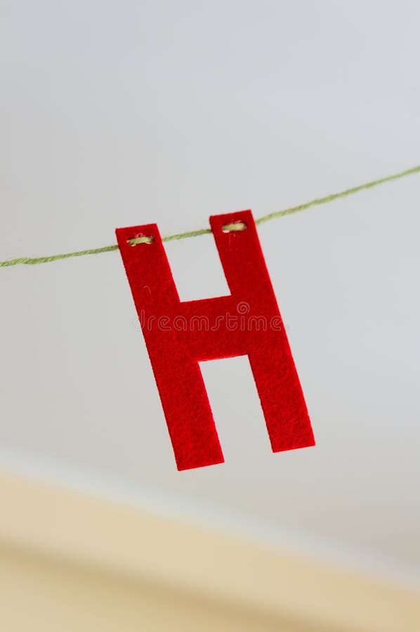 A closeup shot of a red H letter hanging on a cable with a blurred background. A closeup shot of a red H letter hanging on a cable with a blurred background