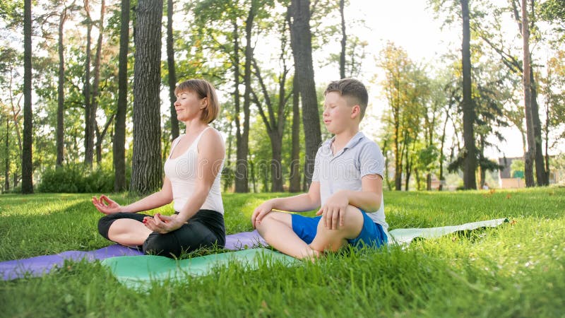 Φωτογραφία της μητέρας με το asana γιόγκας άσκησης γιων εφήβων της στη χλόη στο πάρκο Οικογένεια που κάνει την ικανότητα και τον στοκ φωτογραφίες Φωτογραφία της μητέρας με το asana γιόγκας άσκησης γιων εφήβων της στη χλόη στο πάρκο Οικογένεια που κάνει την ικανότητα και τον στοκ φωτογραφίες