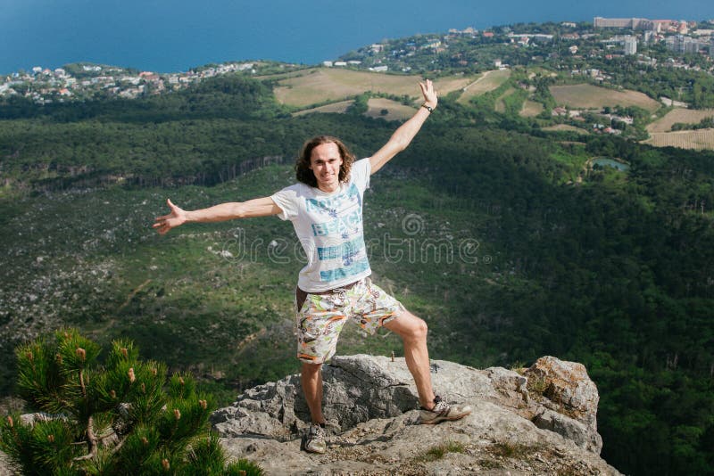 Φωτογραφία του νέου όμορφου ευτυχούς ατόμου που στέκεται πέρα από τα βουνά και που εξετάζει τη κάμερα στοκ φωτογραφία με δικαίωμα ελεύθερης χρήσης Φωτογραφία του νέου όμορφου ευτυχούς ατόμου που στέκεται πέρα από τα βουνά και που εξετάζει τη κάμερα στοκ φωτογραφία με δικαίωμα ελεύθερης χρήσης