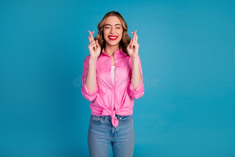 Photo portrait of lovely young lady crossed fingers hope dressed stylish pink garment hairdo isolated on blue color background. Photo portrait of lovely young lady crossed fingers hope dressed stylish pink garment hairdo isolated on blue color background.