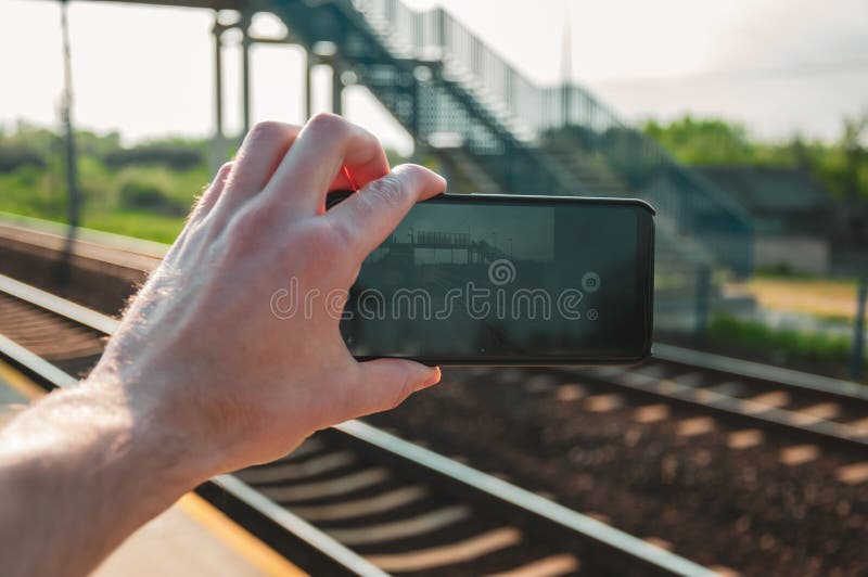 Χέρι ατόμων που κρατά ένα smartphone και που παίρνει μια φωτογραφία του σιδηροδρομικού σταθμού κατά τη διάρκεια της άνοιξη, μεσημ στοκ φωτογραφίες Χέρι ατόμων που κρατά ένα smartphone και που παίρνει μια φωτογραφία του σιδηροδρομικού σταθμού κατά τη διάρκεια της άνοιξη, μεσημ στοκ φωτογραφίες